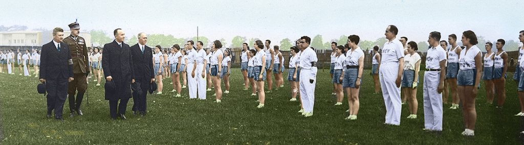 Zawody sportowe Pocztowego Przysposobienia Wojskowego w Krakowie w 1937 r. Trzej urzędnicy i oficer przechodzą przed drużynami sportowymi Fot. NAC